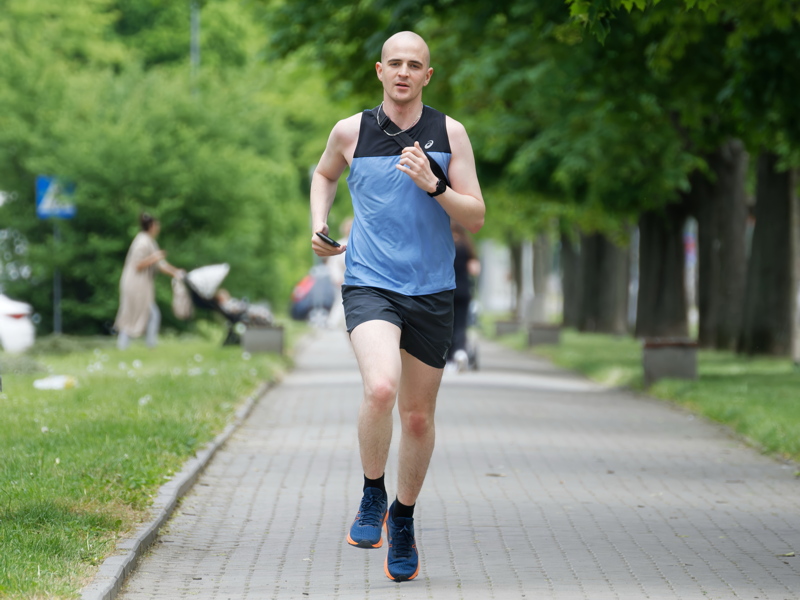 21 - A person jogging outdoors on a paved path wearing a blue sleeveless top and dark shorts